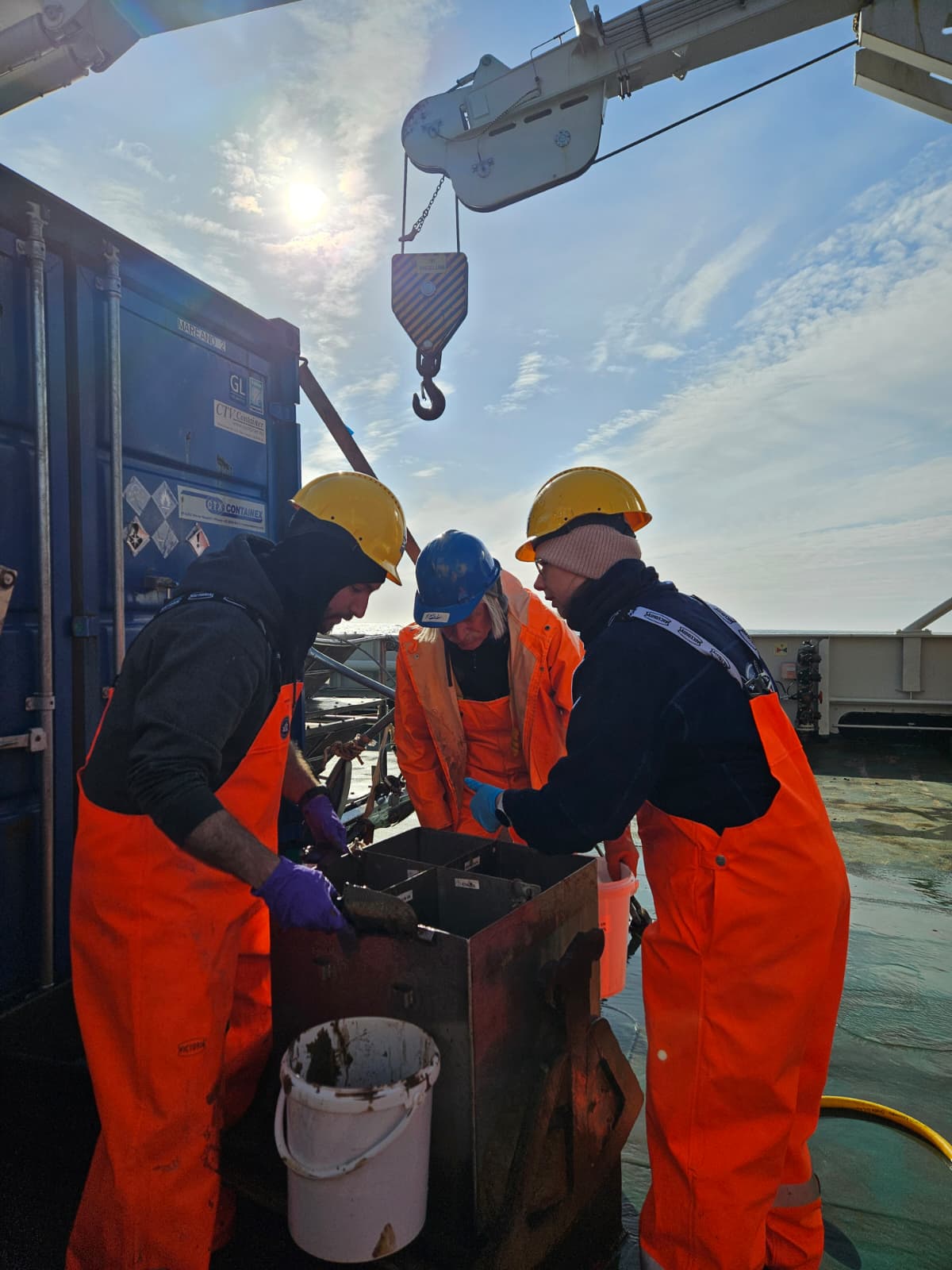 Tre geologer ser ned i en boks. 