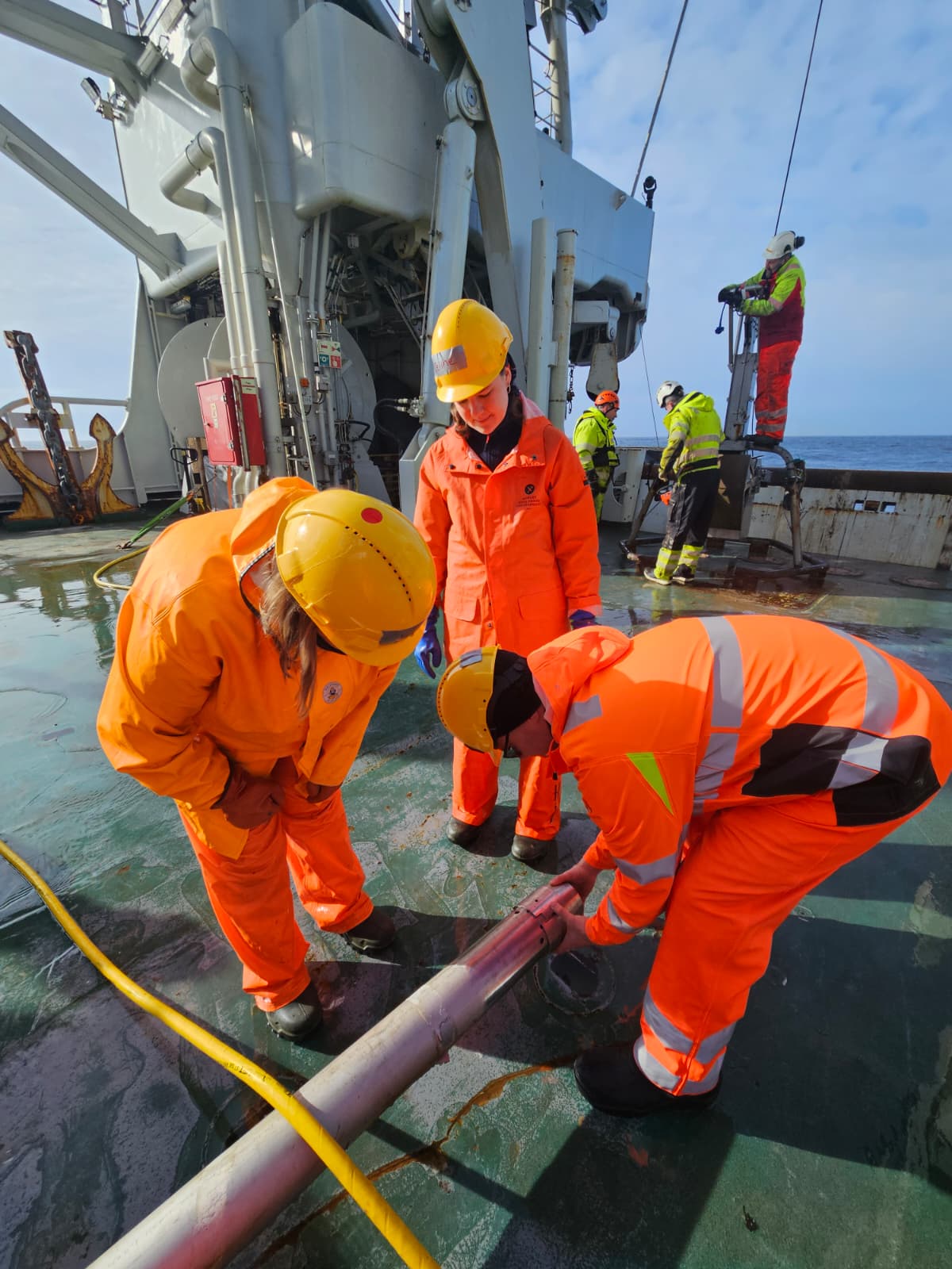 Tre personer ser på et metallrør. Flere andre jobber i bakgrunnen på båten. 