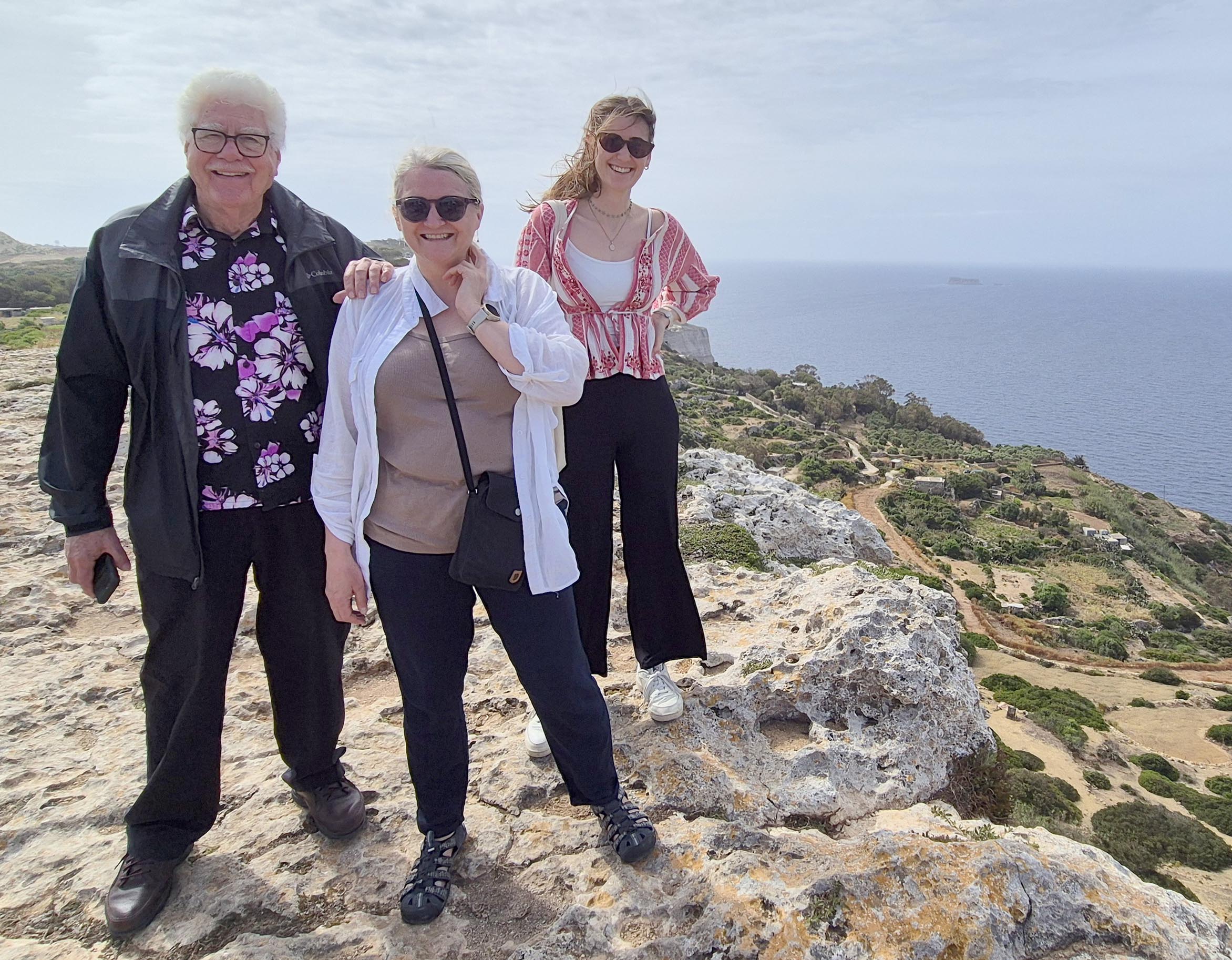 Gary Greene, Lilja Rún Bjarnadóttir og Caroline Gini står på et forsteinet korallrev på toppen av et berg. I bakgrunnen er det en vei i sandfarge og et hav. 