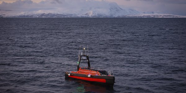 Kongsberg Discovery Sounder USV (ubemanna overflatefartøy) med navnet Frigg ute på havet. Snødekte fjell i bakgrunnen.