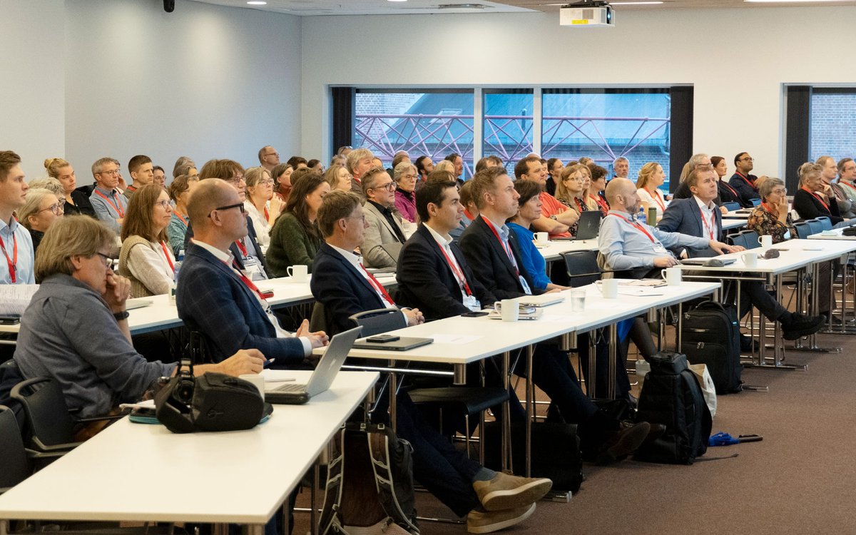 Bilde av publikum som fyller ein sal. Det er omtrent 100 personar på bildet.