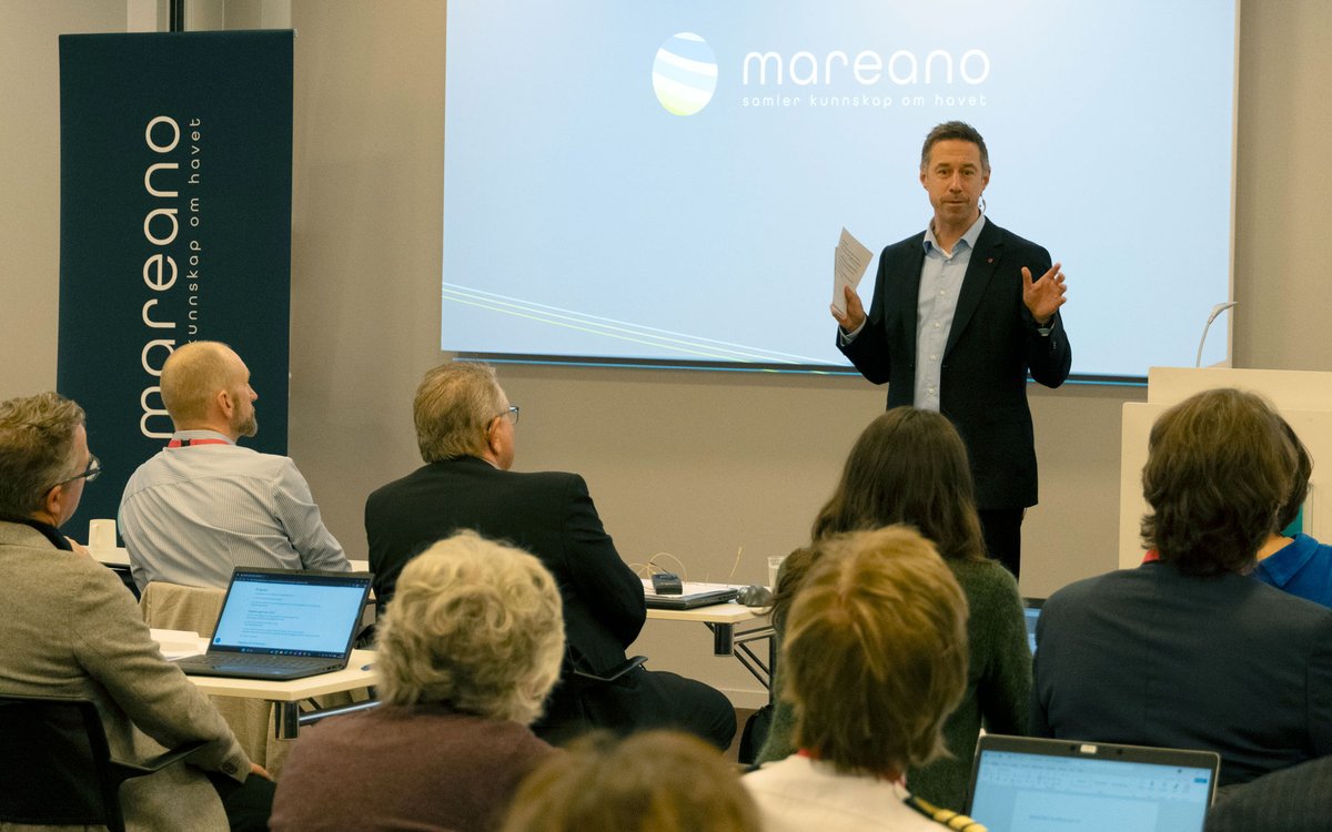 En mann i dress står foran publikum, han er engasjert og snakker til de.