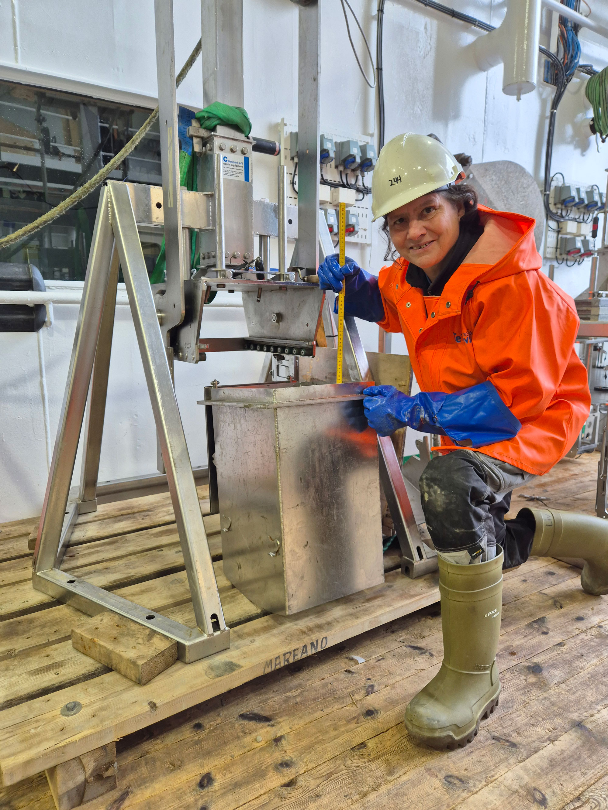 En kvinne med hjelm og regntøy undersøker innholdet i en metallbeholder.