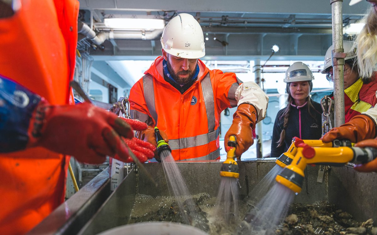 Flere toktdeltakere står rundt en slags stor sil og spyler vekk gjørme.